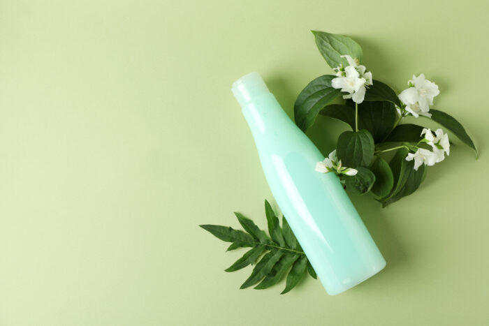Blank bottle of shampoo and flowers on green background