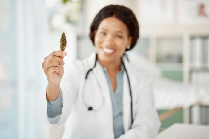 Happy woman doctor with medicinal marijuana or cannabis plant in hand in a healthcare hospital for
