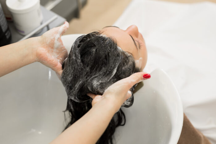 Young girl hairdresser washes her hair with shampoo and massages the head of a young woman in a